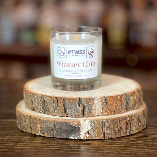 Whiskey CLub scented candle in a rocks glass on top of wood slices